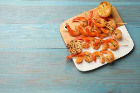 Delicious grilled shrimp skewers, lemon and garlic on light blue wooden table, top view. Space for...