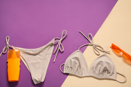 Beige swimsuit, sunglasses and sunscreen on color background, flat lay. Space for textの写真素材