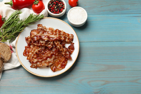Slices of tasty fried bacon, different spices and bread on light blue wooden table, top view. Space...