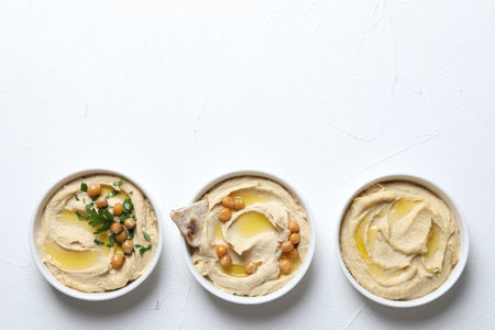 Delicious hummus with olive oil, chickpeas and pita in bowls on light textured table, flat lay. Space for textの写真素材