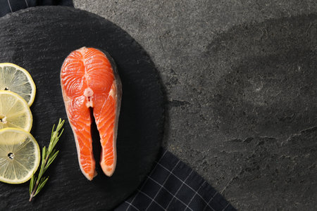 Fresh salmon steak, rosemary and lemon on dark textured table, top view. Space for textの写真素材