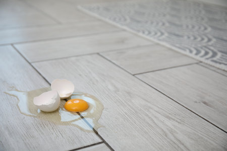Broken raw egg and shell on light gray wooden floor indoors. Space for textの写真素材