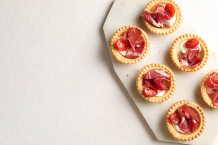 Delicious canapes with jamon, cream cheese and cherry tomatoes on light table, top view. Space for textの写真素材