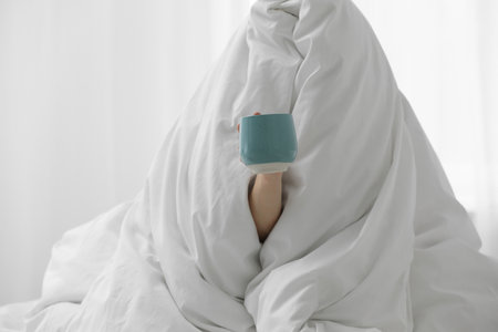 Woman wrapping in blanket sitting with cup of coffee at home. Good morningの写真素材