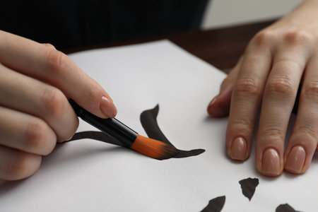 Calligraphy. Woman with brush writing word Entrance in Chinese on paper at table, closeupの写真素材