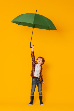 Little boy with green umbrella on orange backgroundの写真素材