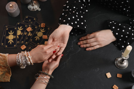 Fortune teller reading lines on woman's palm at black table, top view. Chiromancyの写真素材
