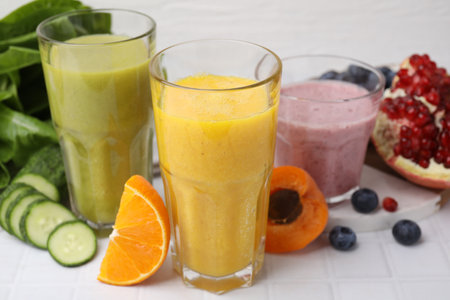 Tasty smoothies in glasses and ingredients on white tiled table, closeupの写真素材