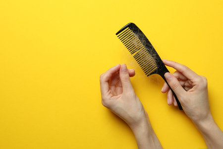 Woman taking her lost hair from comb on yellow background, top view. Space for textの写真素材