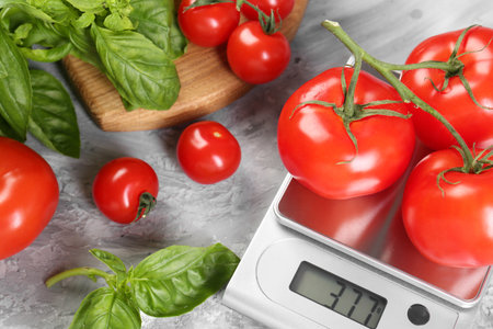 Kitchen scale with tomatoes and basil on gray textured table, closeupの写真素材