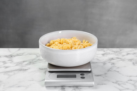 Kitchen scale with bowl of pasta on white marble table