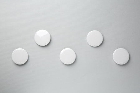 Blank white button badges on grey background, top view. Mockup for design