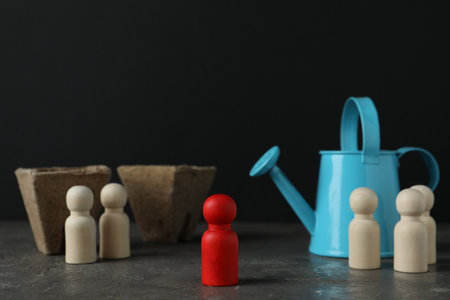 Different human figures, watering can and soil on gray textured table against dark background