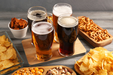 Glasses with different types of beer and snacks on gray wooden table