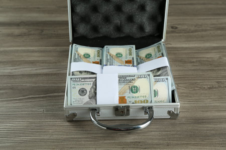 Metal case full of dollar banknotes at wooden table