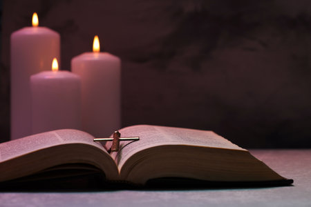 Cross, Bible and burning candles on textured table against dark background, closeup. Religion of...