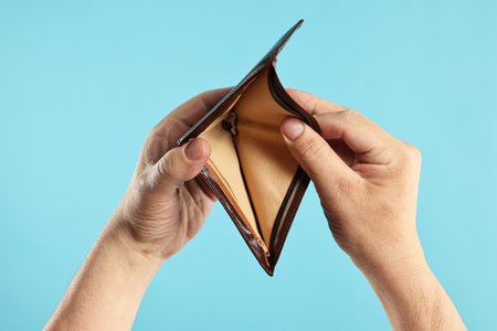 Man with empty wallet on light blue background, closeup