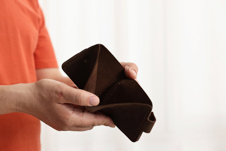 Man with empty wallet on blurred background, closeup. Space for text
