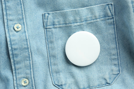 White button badge pinned on denim shirt, top view. Mockup for designの写真素材