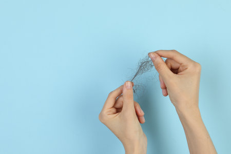 Woman holding lost hair on light blue background, closeup. Space for textの写真素材