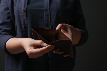 Woman with empty wallet on dark background, closeup