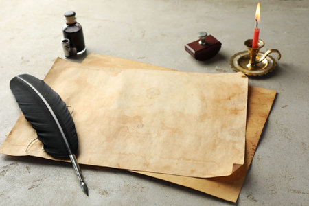 Sheet of old parchment paper, black feather, inkwell and candle on gray tableの写真素材