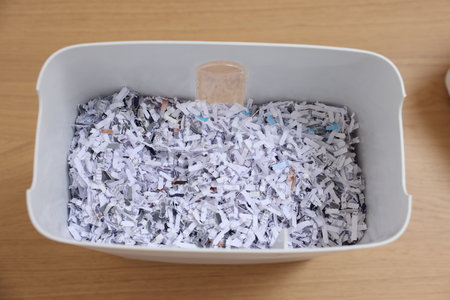 Shredded paper strips in bin on wooden table, top view