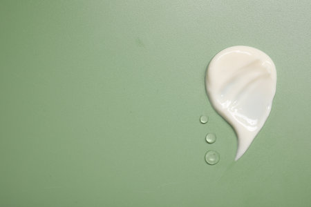 Face cream and gel on green background, top view. Space for text