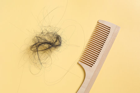 Wooden comb with lost hair on yellow background, top viewの写真素材