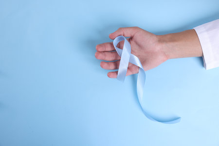 Prostate cancer awareness. Man with light blue ribbon as symbol of support on color background, top...