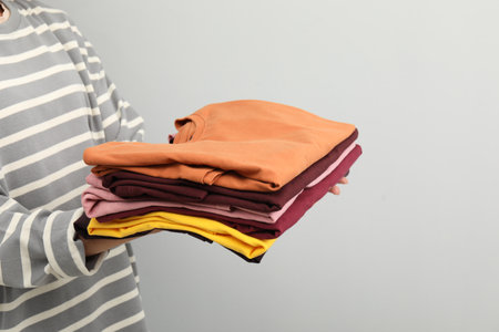 Woman with stack of clothes on gray background, closeup. Space for text