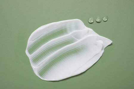 Face cream and gel on green background, top view