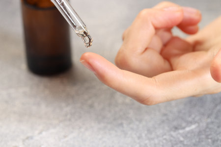 Woman dripping essential oil onto finger at gray table, closeupの写真素材