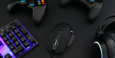 Computer mouse, headset, RGB keyboard and game controllers on black background, closeup