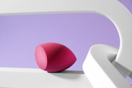 Stylish presentation of makeup sponge on violet background
