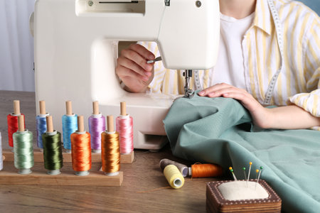 Seamstress working with sewing machine at wooden table indoors, closeupの写真素材