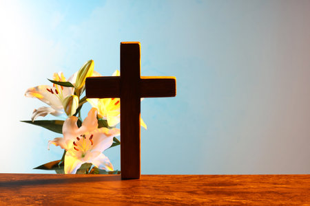 Wooden cross and beautiful lily flowers on table against light blue background, space for text. Religion of Christianityの写真素材