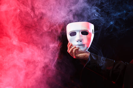 Theatrical performance. Man with plastic mask in smoke on dark background, closeup. Space for textの写真素材