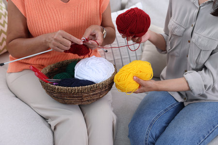 Mother knitting while her daughter holding yarns on sofa, closeup