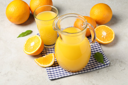 Tasty orange juice in jug, glass and citrus fruits on light textured tableの写真素材