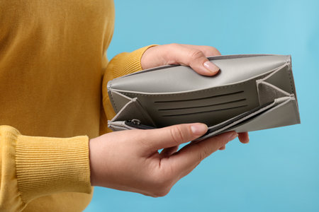 Woman with empty wallet on light blue background, closeup