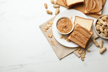 Delicious sandwiches with peanut butter and fresh nuts on white marble table, flat lay. Space for...
