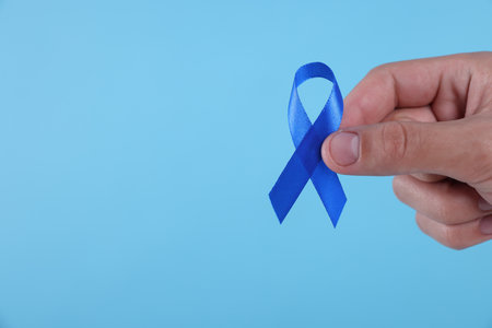 Prostate cancer awareness. Man holding blue ribbon as symbol of support on color background, closeup. Space for textの写真素材