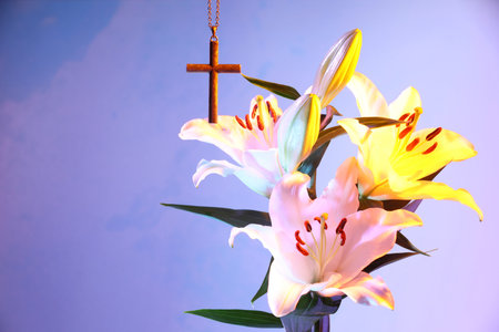 One cross with chain and beautiful lily flowers on violet background, space for text. Religion of...