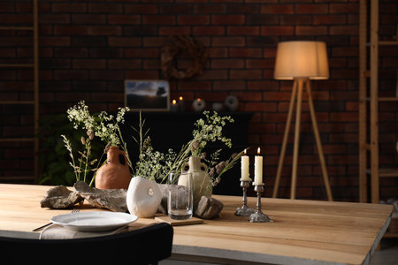 Set of clean dishware, vases with beautiful flowers, stones and burning candles on wooden table in...