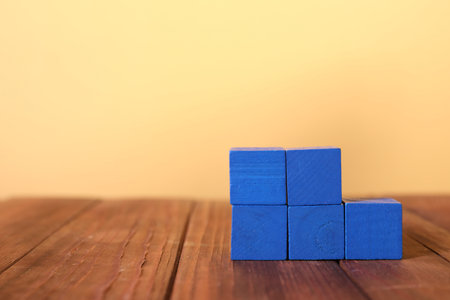Blank colorful cubes on wooden table against pale yellow background, space for text