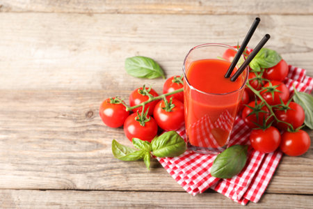 Tasty tomato juice in glass with basil leaves and fresh vegetables on wooden table, space for textの写真素材