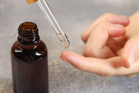 Woman dripping essential oil onto finger at gray table, closeup