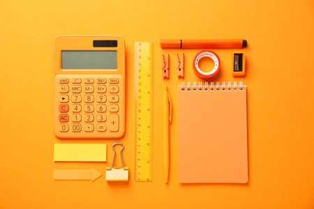 Different stationery on orange background, flat lay