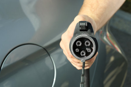 Man holding power supply cable near car at electric vehicle charging station, closeupの写真素材